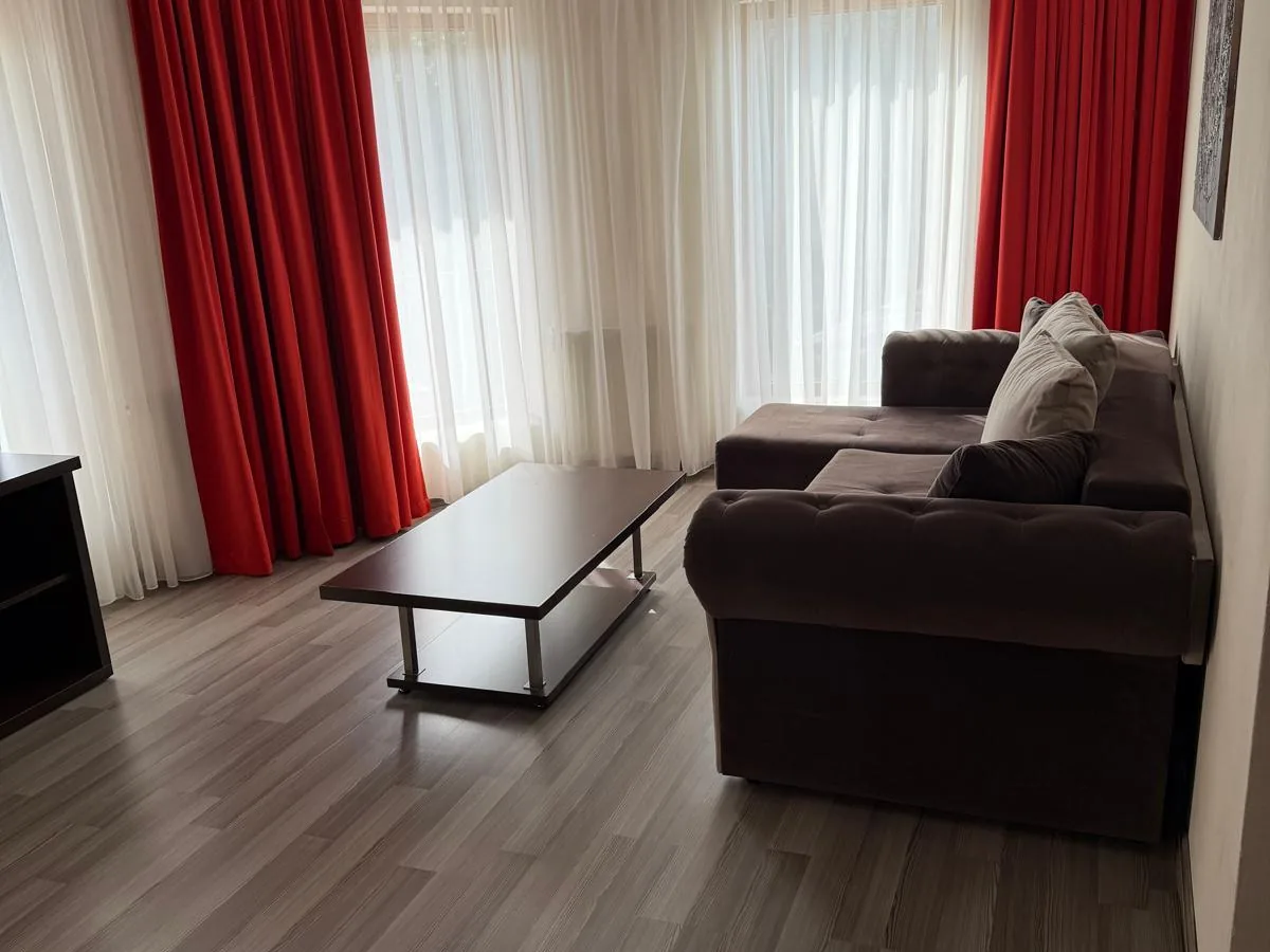 Livingul apartamentului, cu draperii roșii, canapea și măsuță