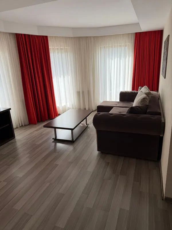 Livingul apartamentului, cu draperii roșii, canapea și măsuță