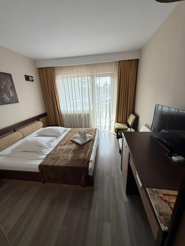 Cameră dublă cu pat matrimonial, perdele aurii și ușă spre balcon
